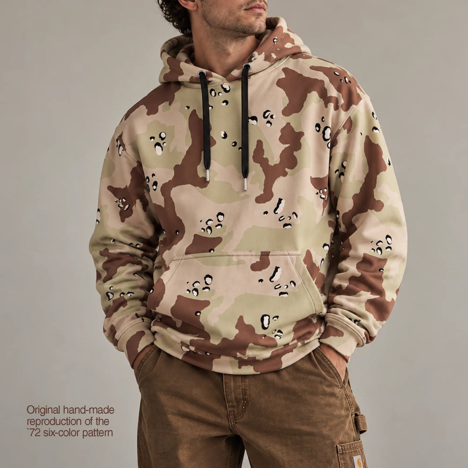 Six-color desert camouflage hoodie worn with brown workwear pants in a neutral studio