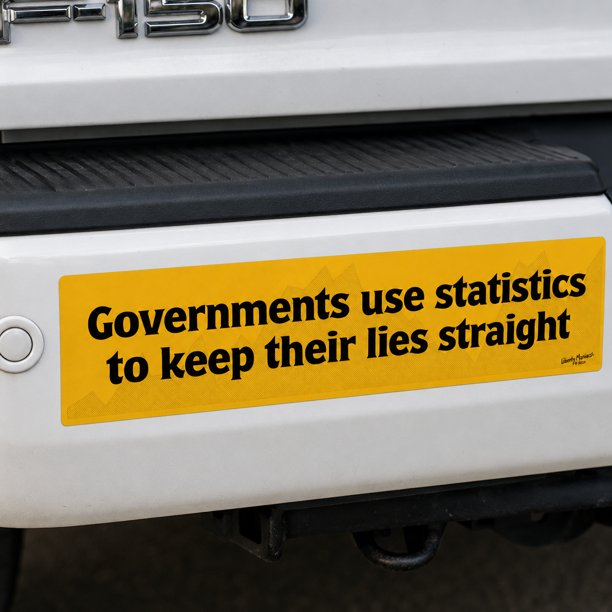 A yellow rectangular bumper sticker with black text reading 'Governments use statistics to keep their lies straight' applied to the rear bumper of a white pickup truck.