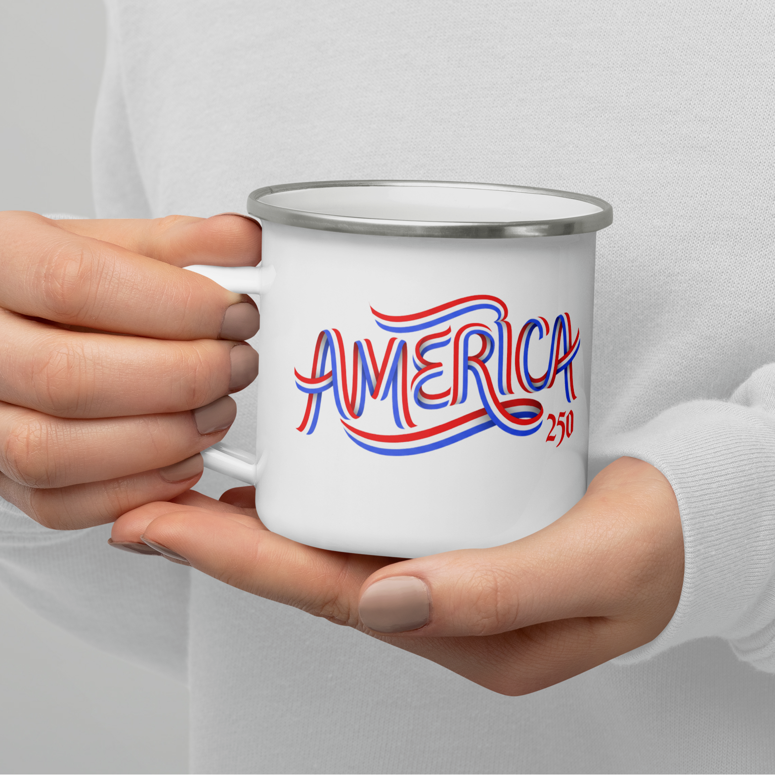 A person in a white long-sleeve shirt holds a white enamel-style mug with a silver rim. The mug has a red and blue script graphic reading “AMERICA 2030.