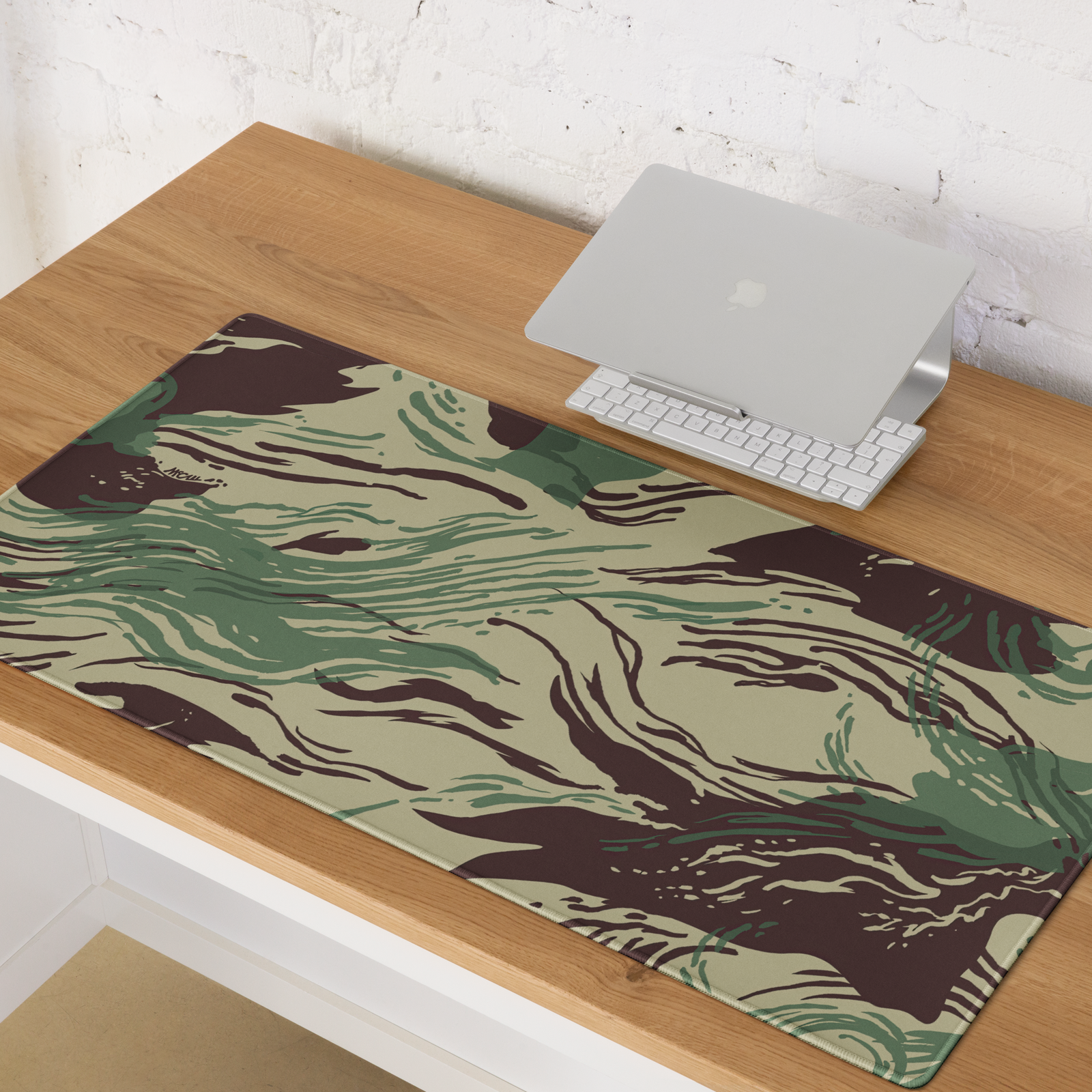 Camouflage-patterned desk mat on a wooden desk with a laptop and keyboard.