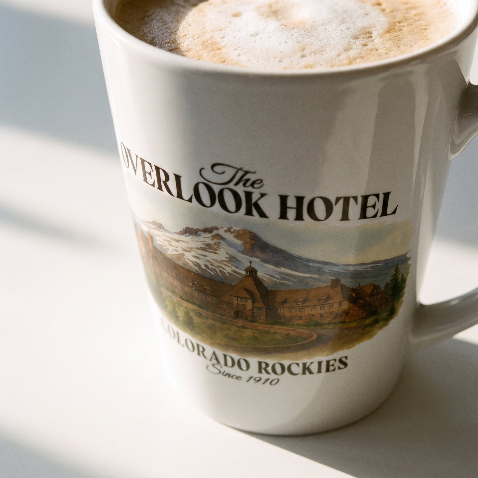 Close-up of the vintage Overlook Hotel Colorado Rockies design on a white latte mug