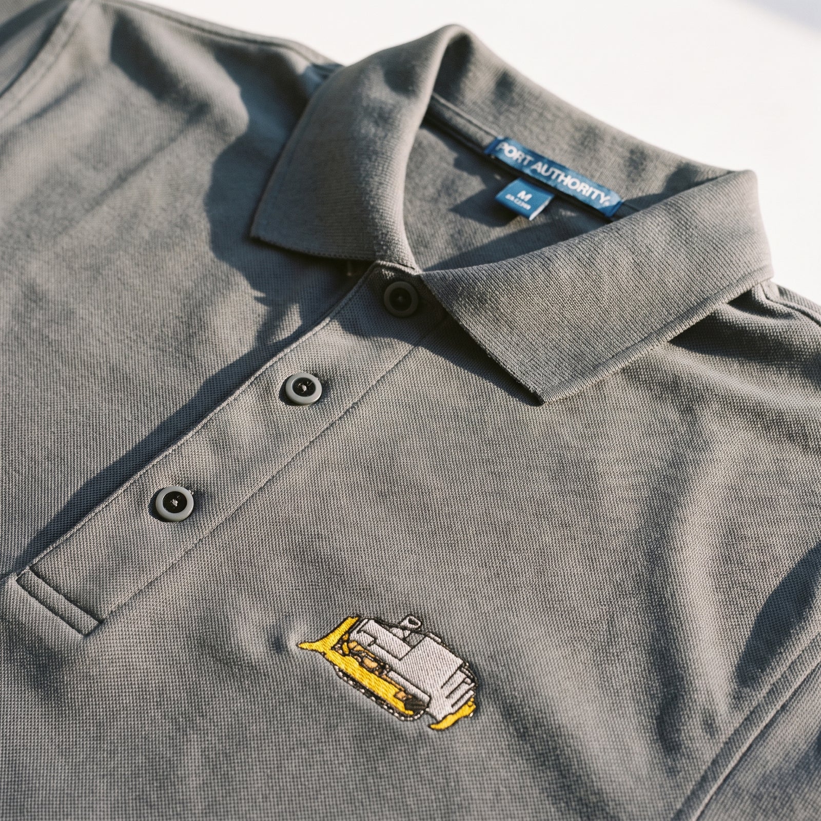 Close-up of a dark gray polo shirt with a small embroidered Killdozer logo on the chest