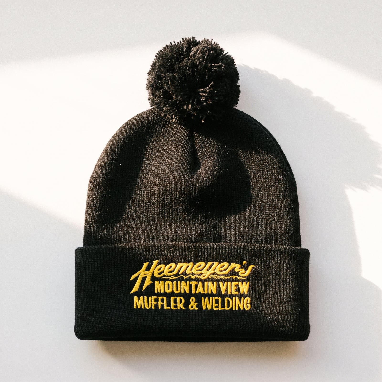 Black Heemeyer’s Mountain View Muffler embroidered pom-pom beanie, full flat lay on white