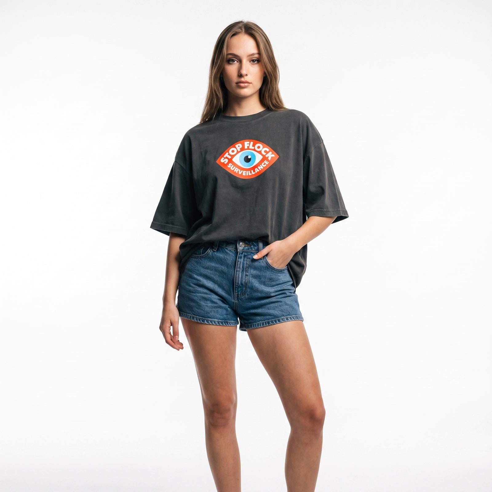 A woman modeling a dark charcoal gray oversized t-shirt with a colorful 'Stop Flok Football' graphic on the chest, paired with blue denim shorts, against a plain white studio background.