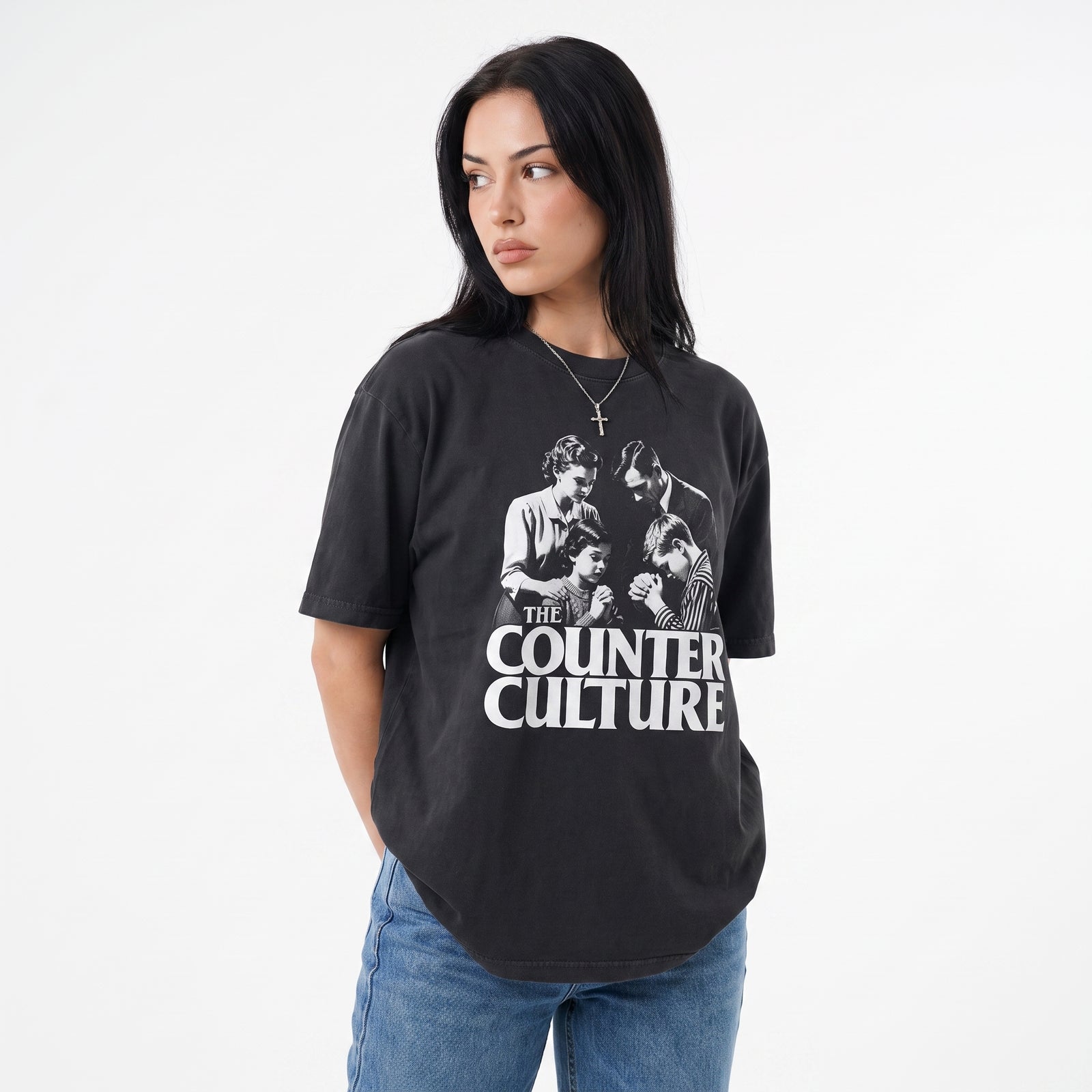 A woman wearing a black graphic t-shirt with a white print of the band 'The Counter Culture' and blue jeans, photographed against a plain white background.