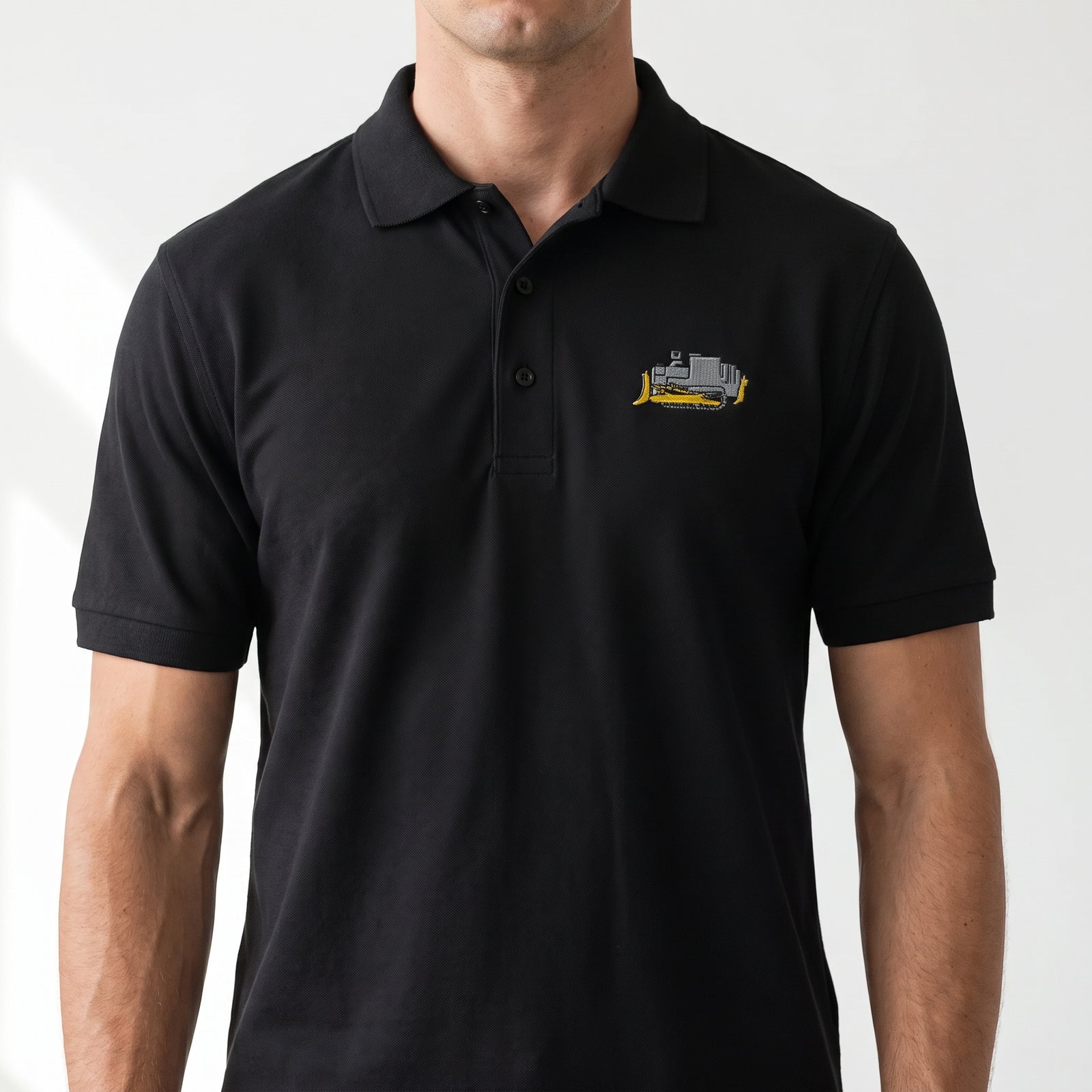 A man wearing a black short-sleeve polo shirt with a small embroidered killdozer on the left chest, shown against a plain light background.