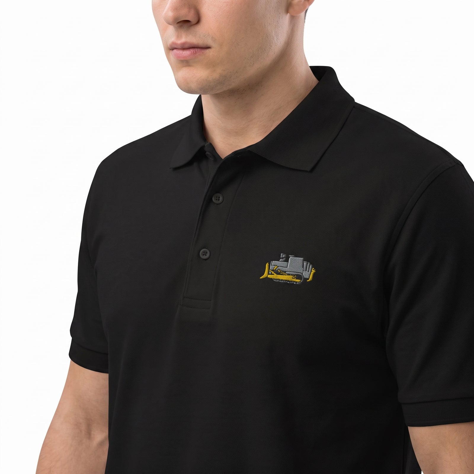 A man wearing a black short-sleeve polo shirt with a small embroidered bulldozer logo on the left chest, set against a plain white background.