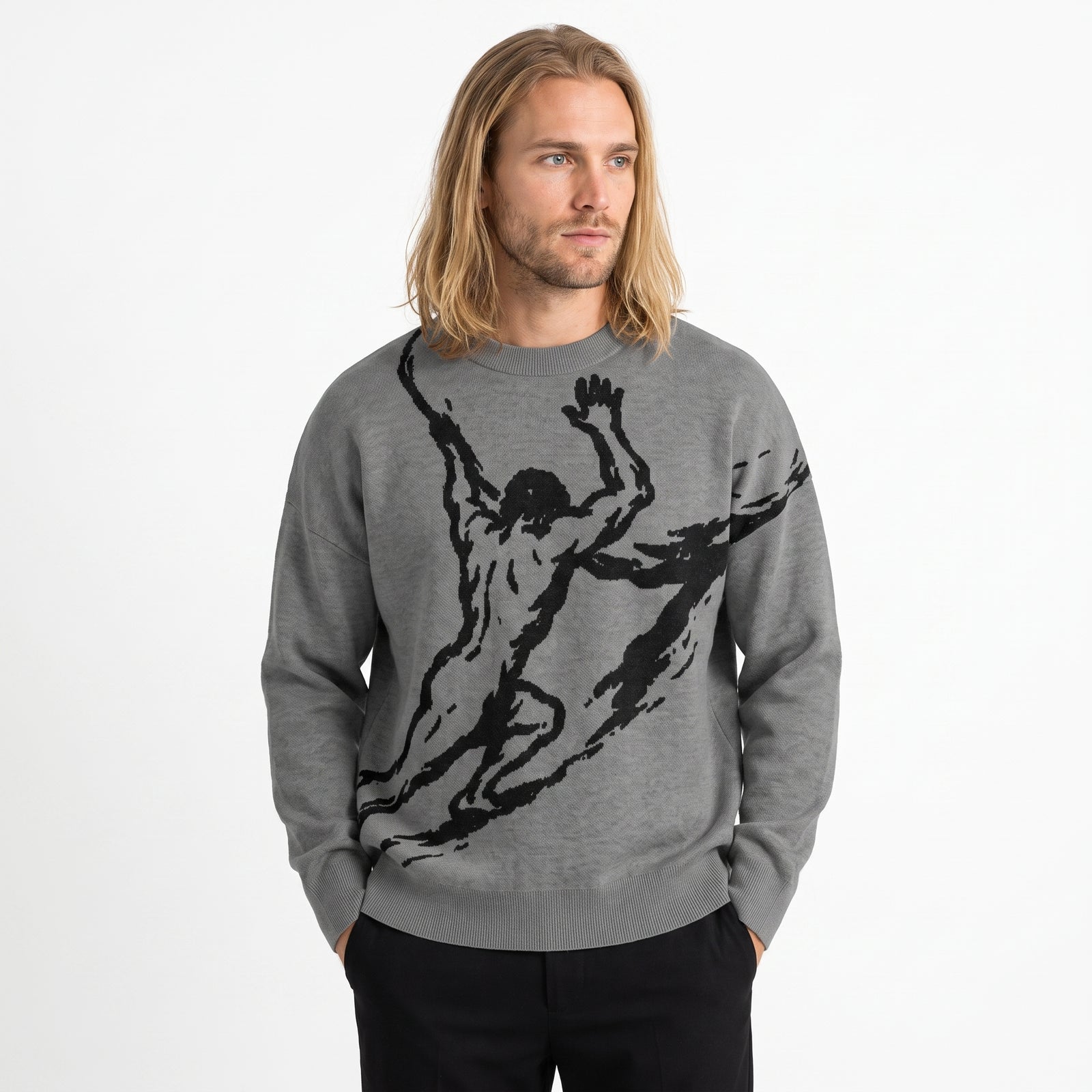 A man with long blonde hair wearing a heather gray crewneck sweater with a large black graphic of a muscular Sisyphus, paired with black pants, against a plain white background.