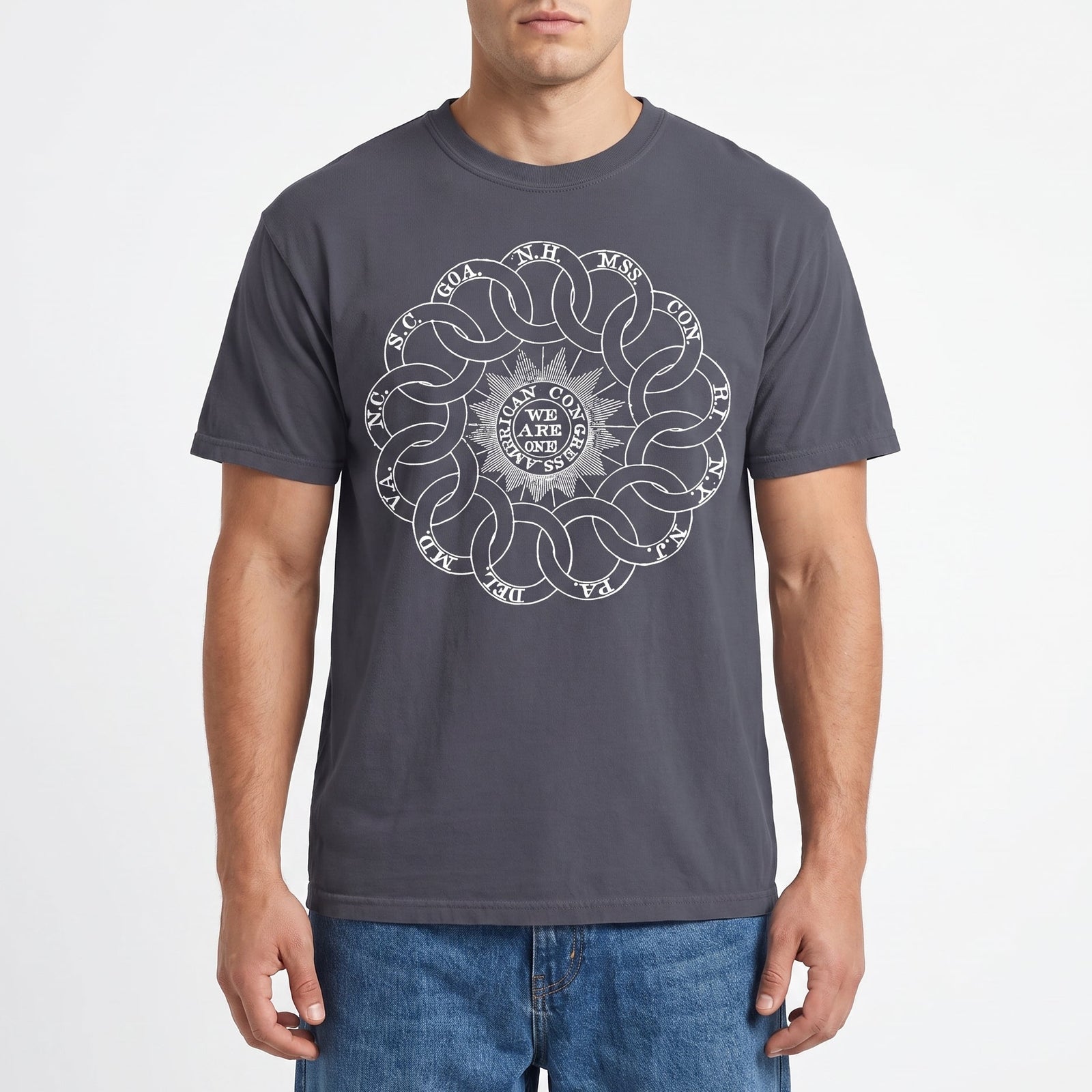 A man wearing a dark gray crewneck t-shirt with a white circular mandala-style graphic on the chest, paired with blue jeans, against a light gray studio background.