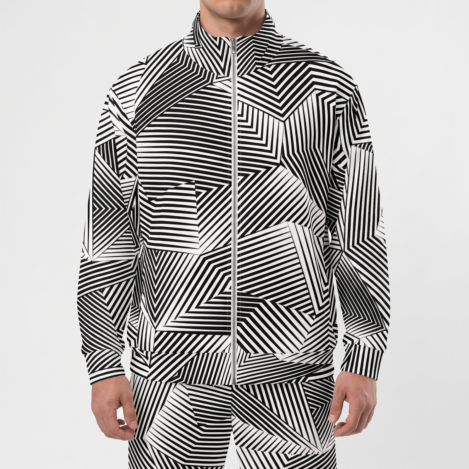 A man wearing a black and white geometric patterned zip-up jacket and matching pants against a light gray studio background.