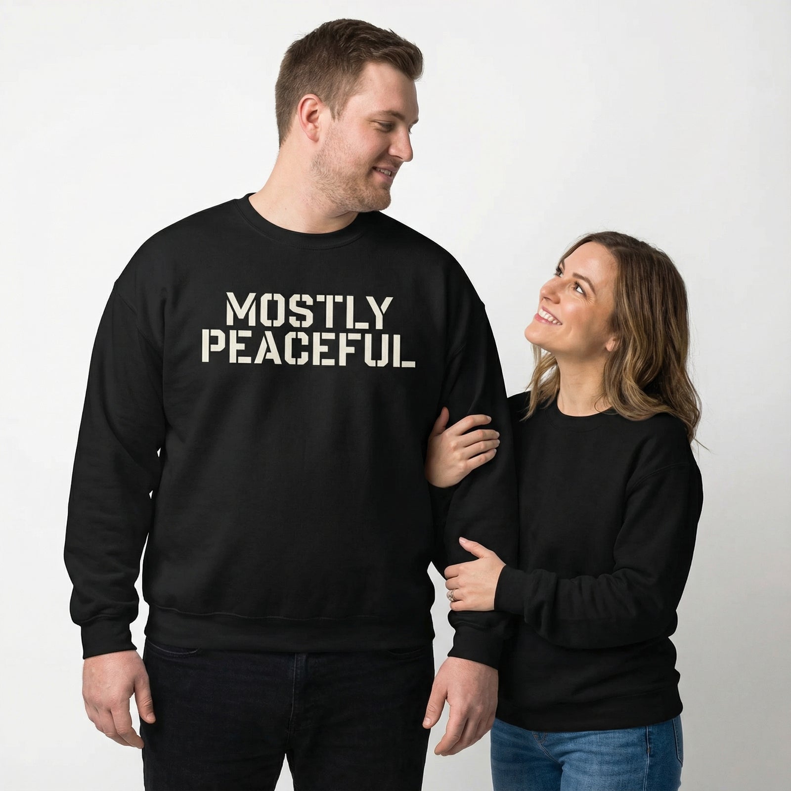 Two people wearing black sweatshirts with 'MOSTLY PEACEFUL' text on a plain background
