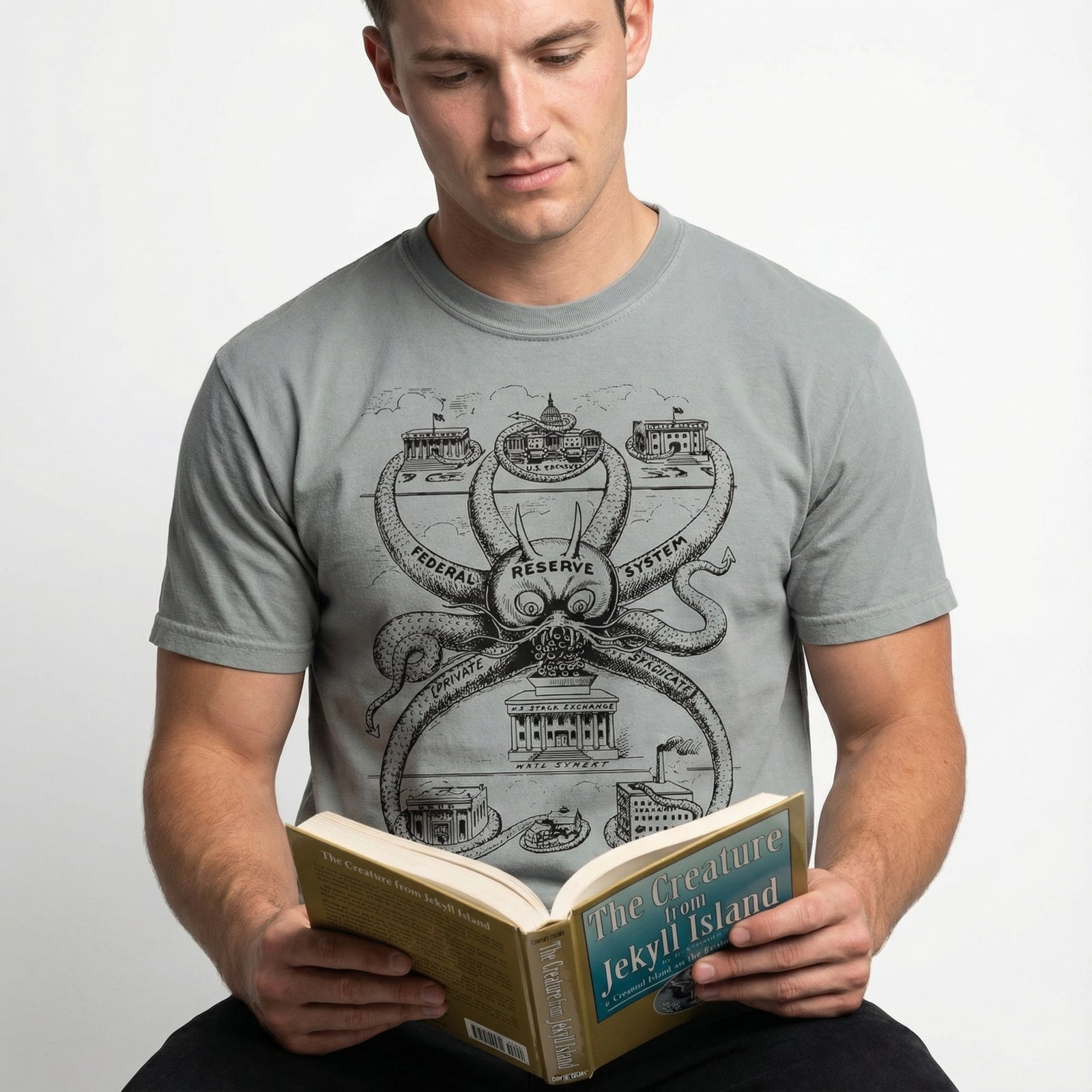 Man wearing a t-shirt with a graphic design, holding a book titled 'The Creature from Jekyll Island'.