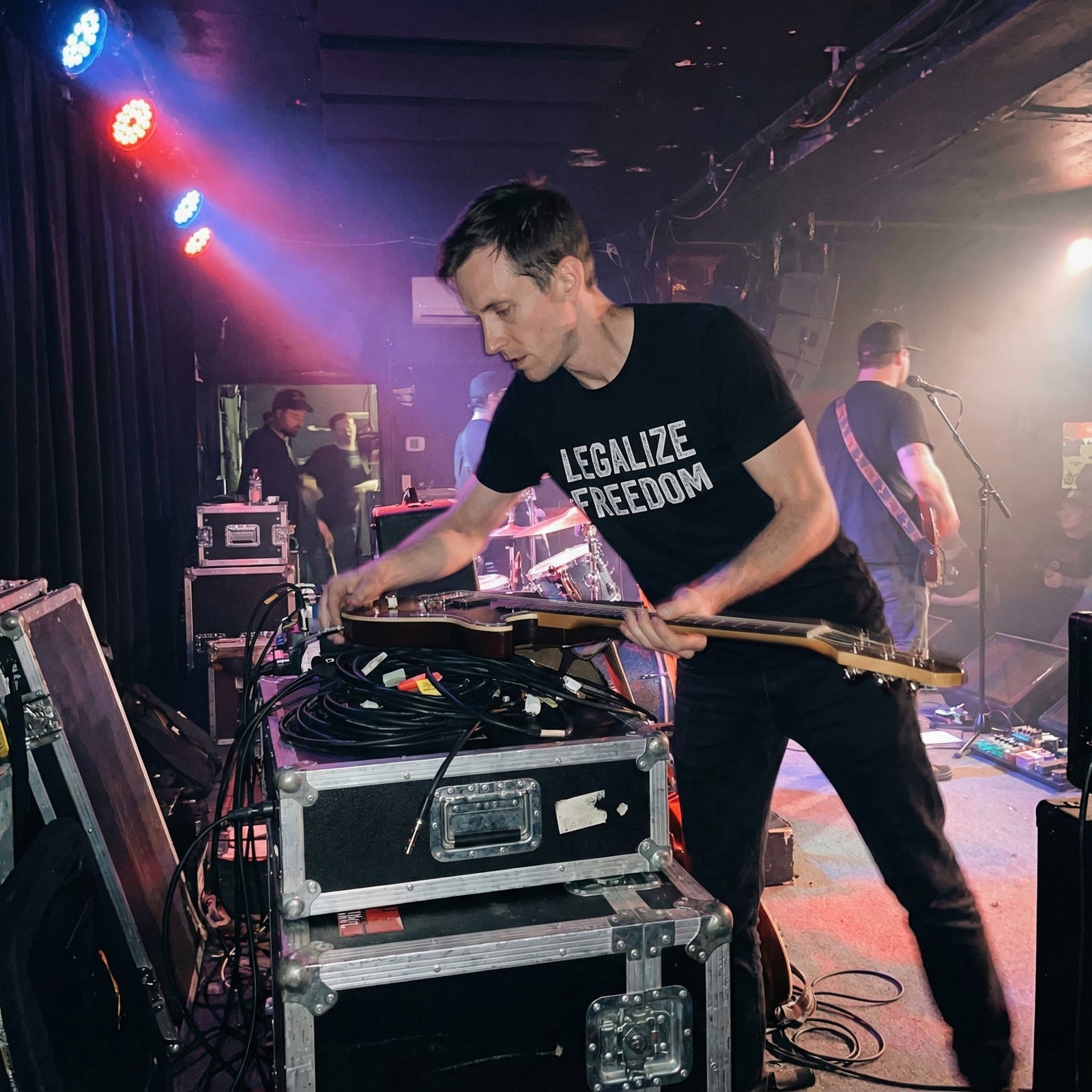 Person playing guitar on stage with equipment and lighting in the background