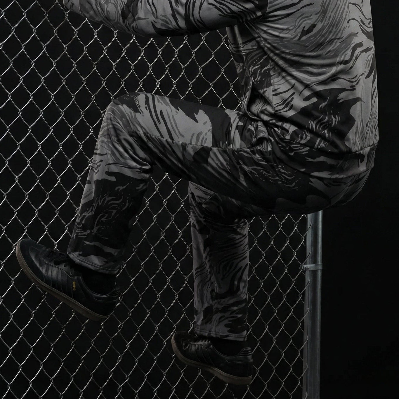 Person in tactical gear climbing a chain-link fence against a dark background