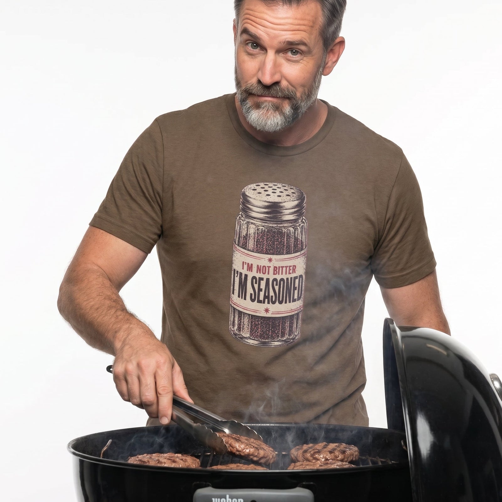 Man grilling burgers wearing a t-shirt with a seasoning jar graphic.