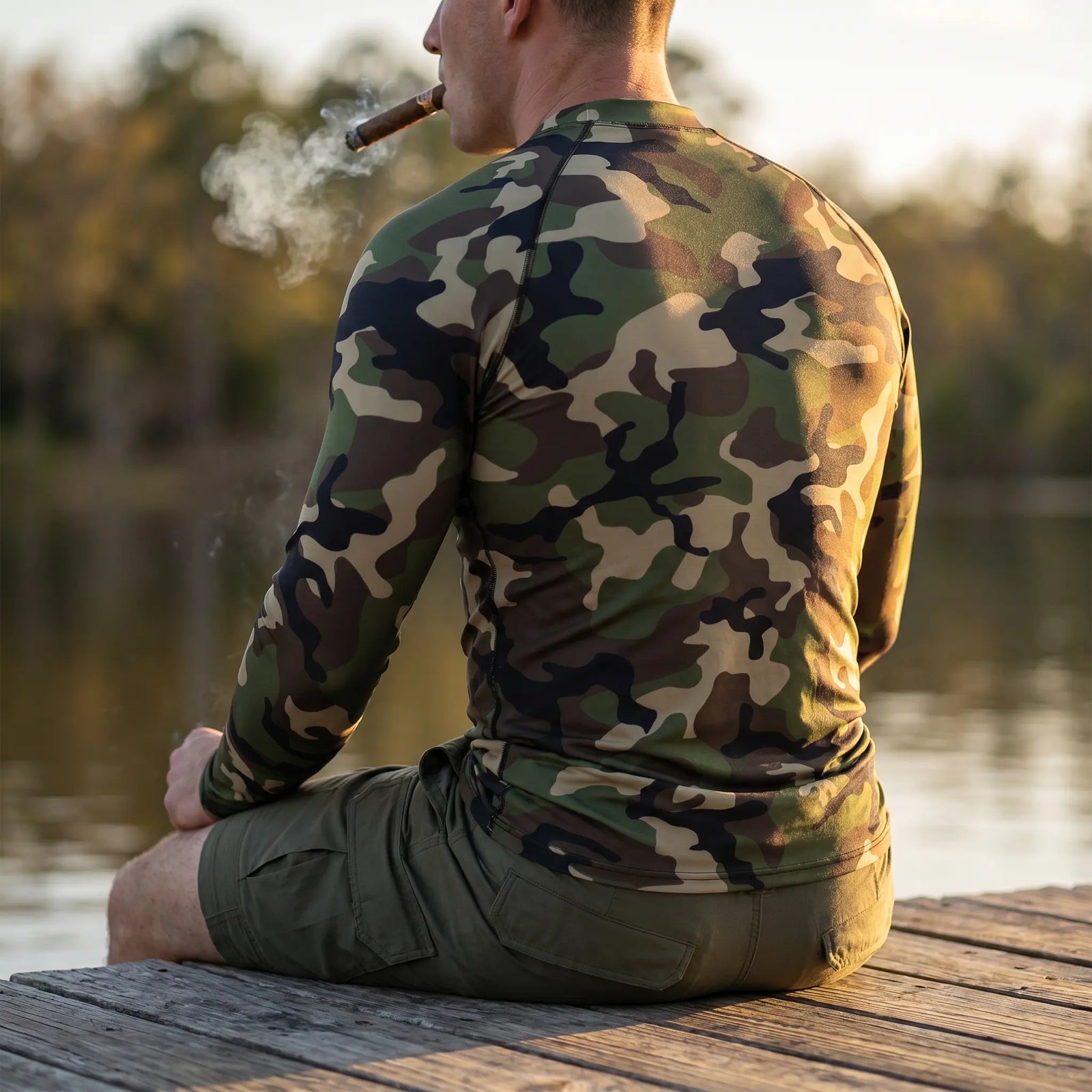 Person wearing a camouflage shirt sitting on a dock by a body of water.