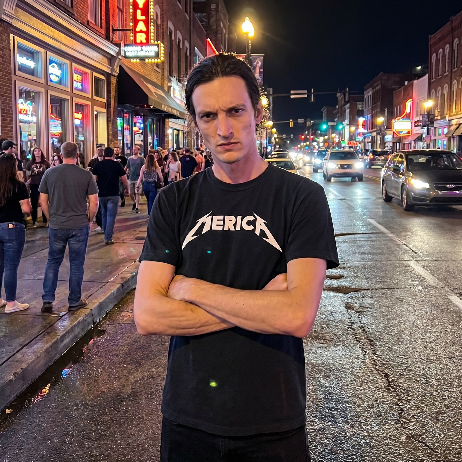 Person wearing a black t-shirt with a 'MERICA' logo on a city street at night