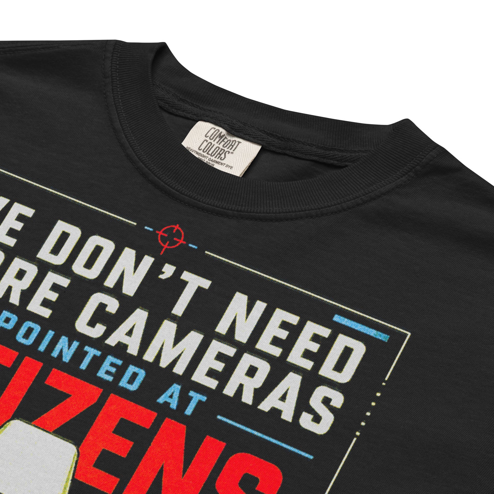 Cameras Pointed at Politicians Heavyweight Graphic Tee featuring a spy movie style surveillance camera aimed at the U.S. Capitol with bold red, cream, and blue typography on a black shirt.
