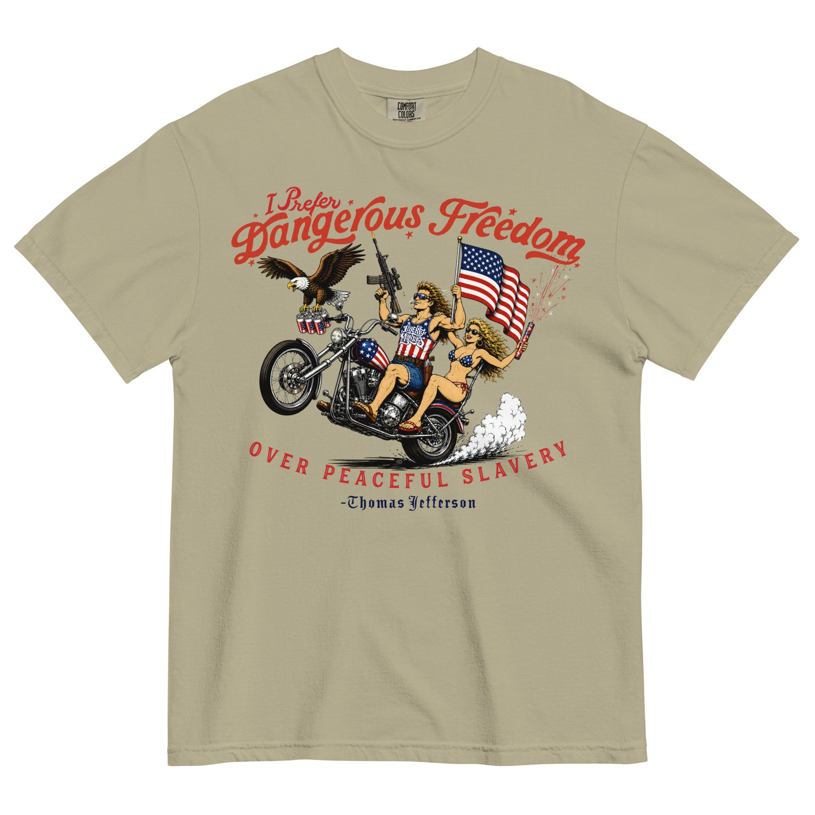 A beige short-sleeve t-shirt featuring a retro-style illustration of a man and women on a motorcycle with American flags, an eagle, and fireworks. Red text above reads 'I Prefer Dangerous Freedom' and text below reads 'OVER PEACEFUL SLAVERY -Thomas Jefferson'. By Liberty Maniacs