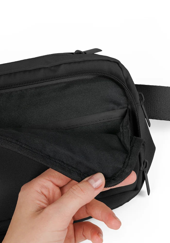 Black waist bag being held open by a hand on a white background