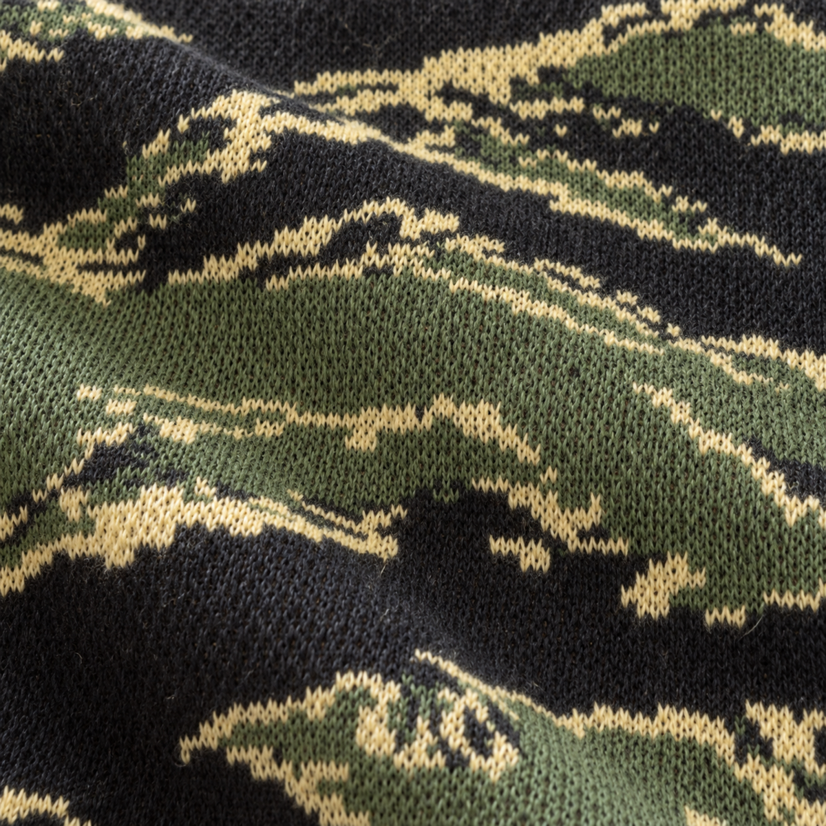 Close-up of black, olive green, and pale yellow tiger-stripe jacquard sweater, showing fine knit stitches and soft fabric folds.