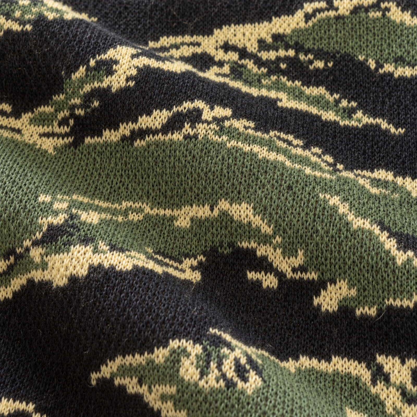 Close-up of black, olive green, and pale yellow tiger-stripe jacquard sweater, showing fine knit stitches and soft fabric folds.