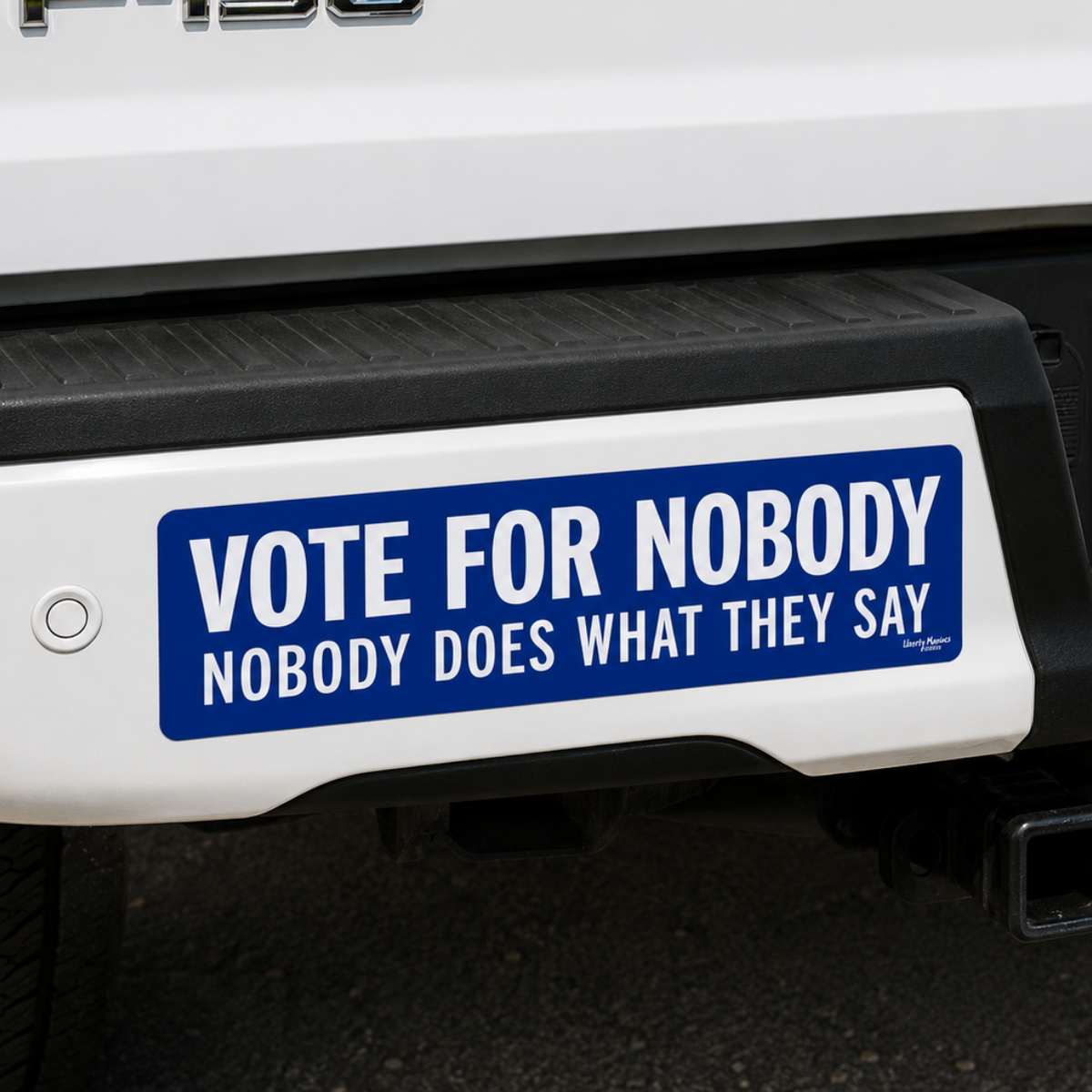 A blue and white bumper sticker with the text 'VOTE FOR NOBODY NOBODY DOES WHAT THEY SAY' applied to the rear bumper of a white Ford F-150 truck.