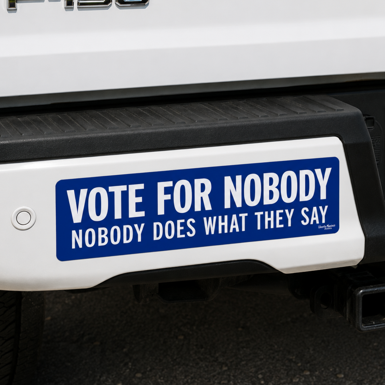 A blue and white bumper sticker with the text 'VOTE FOR NOBODY NOBODY DOES WHAT THEY SAY' applied to the rear bumper of a white Ford F-150 truck.
