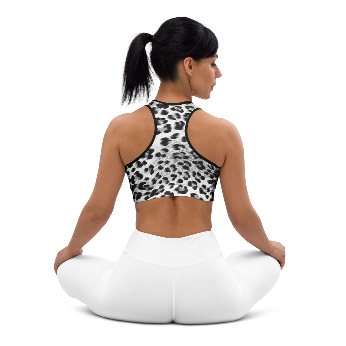 Woman sitting on a white yoga ball wearing a leopard print sports bra and white pants on a white background
