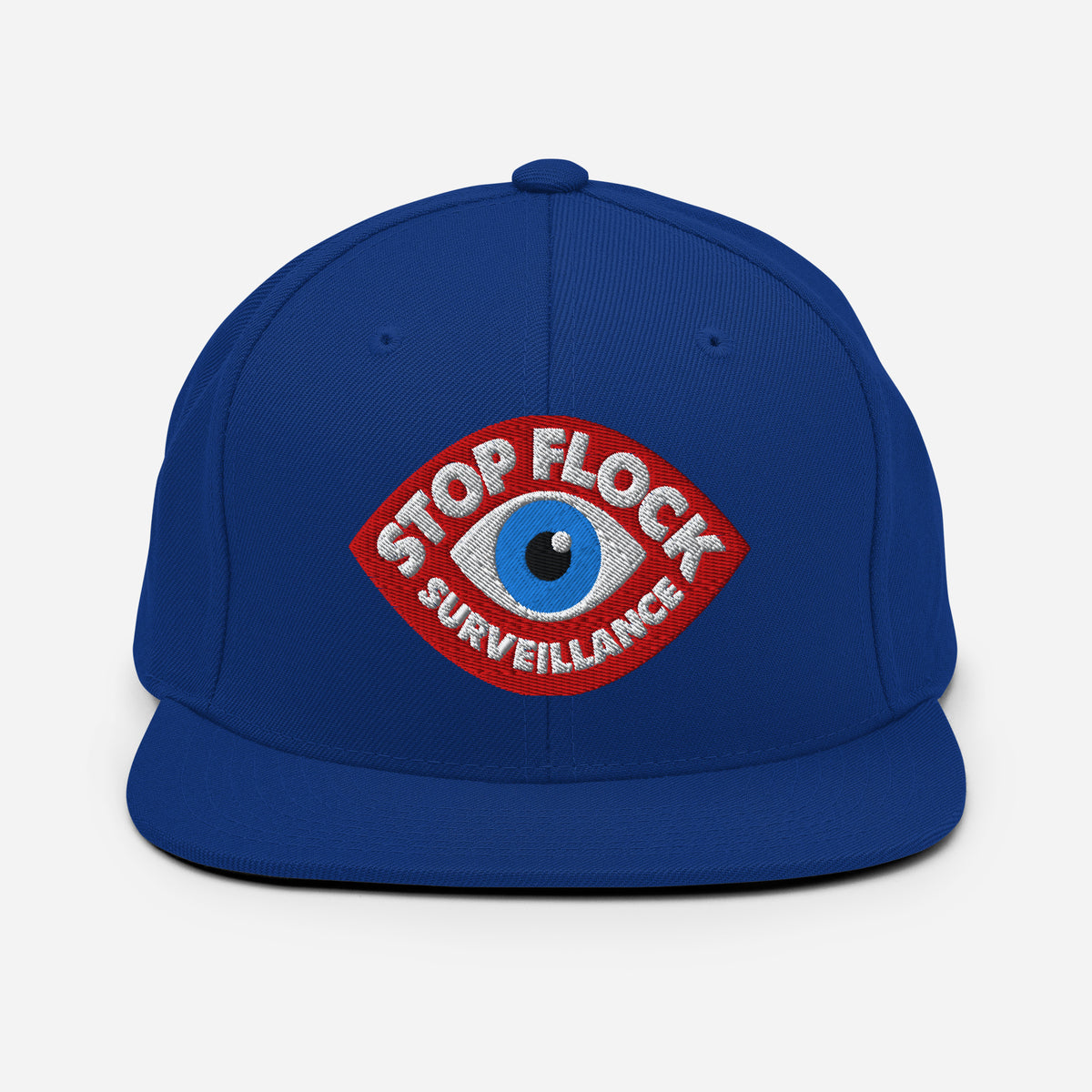 A royal blue flat-brim snapback cap featuring a red and white embroidered patch with a blue eye and the text 'STOP FLOCK SURVEILLANCE' on the front.