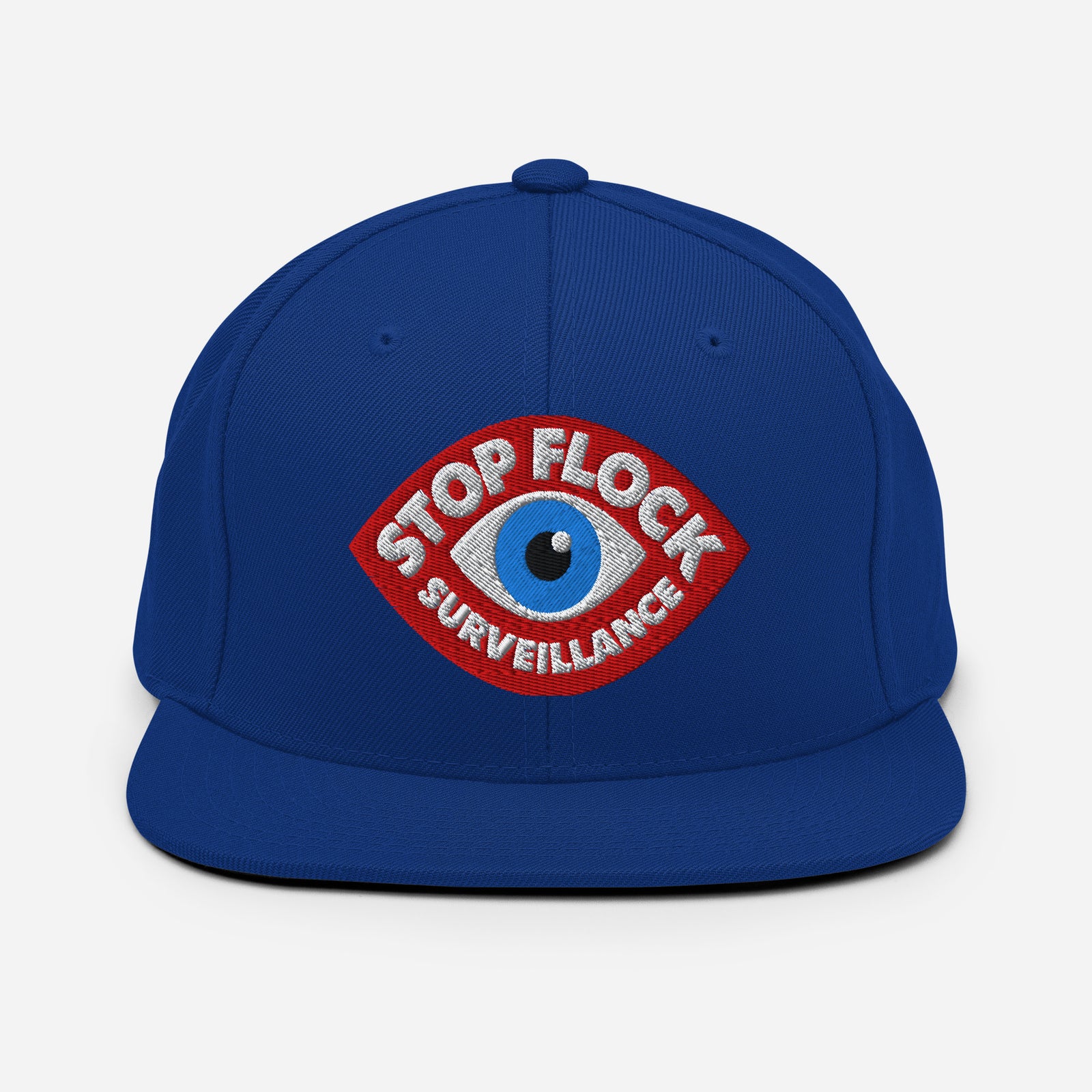 A royal blue flat-brim snapback cap featuring a red and white embroidered patch with a blue eye and the text 'STOP FLOCK SURVEILLANCE' on the front.