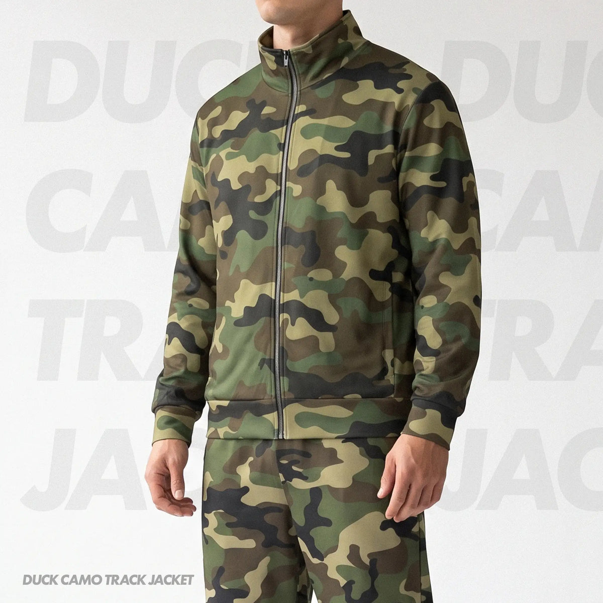 A man wearing a green camouflage full-zip track jacket and matching track pants, shown from the neck down against a light gray background with a subtle watermark.