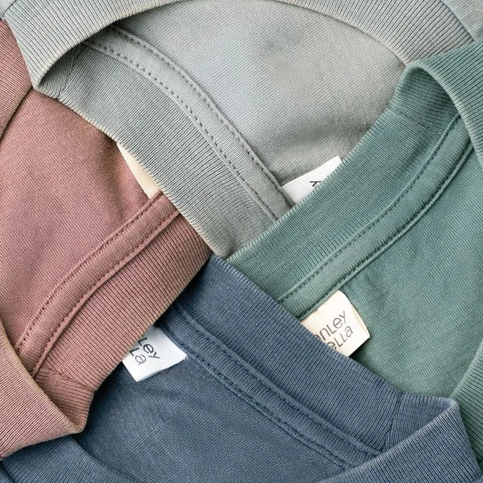 Close-up of folded organic cotton garment dyed t-shirts from Liberty Maniacs in various colors with a brand label.