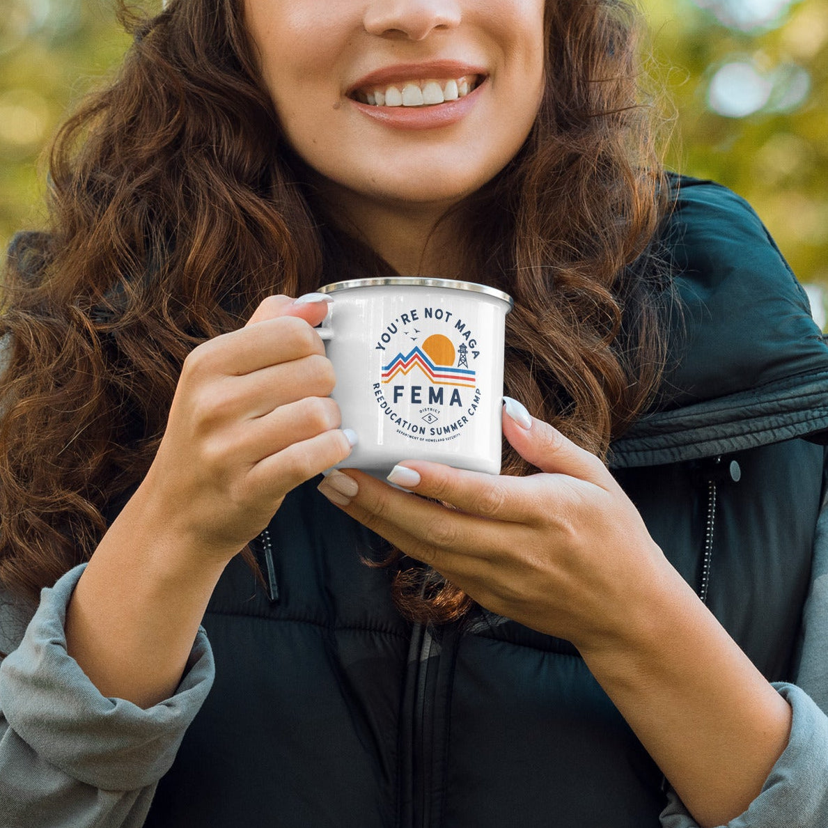Woman holding a silver cup with a logo, wearing a beige beanie and dark jacket, outdoors.