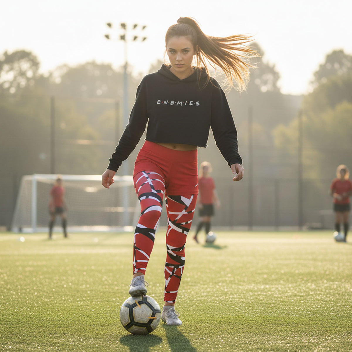 Woman in black sweatshirt and red leggings with soccer ball on a field