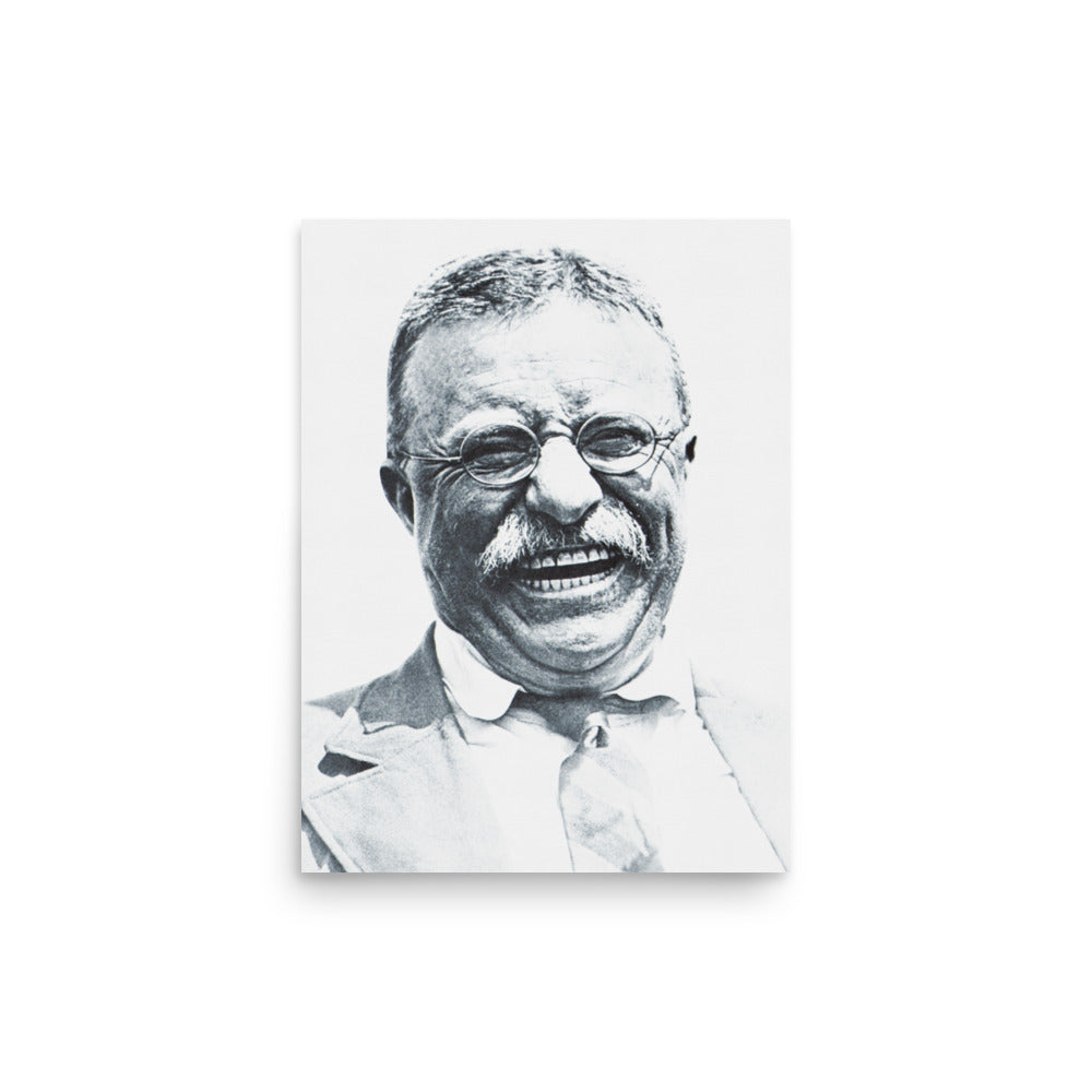 A framed black and white portrait print of a smiling man with glasses, displayed on a dark wall above a brown leather armchair in a styled room with a brass lamp and books.