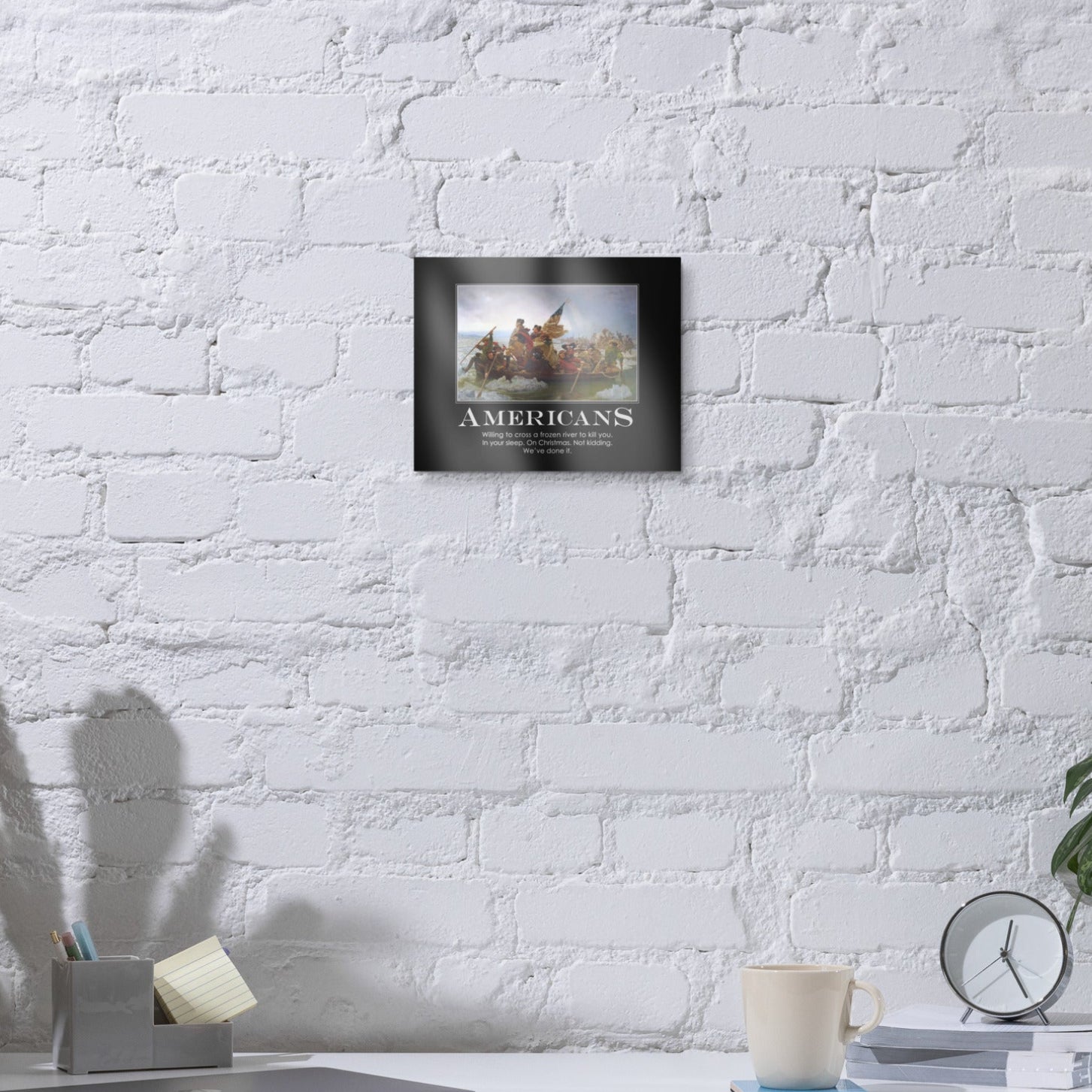 Framed picture on a white brick wall above a desk with office items.