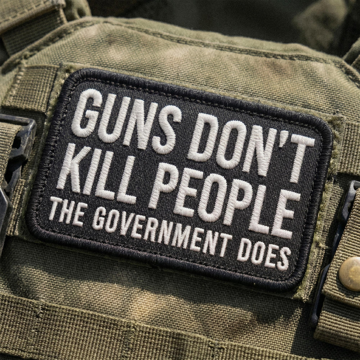 Patch on a green tactical vest with text 'Guns don't kill people, the government does'.