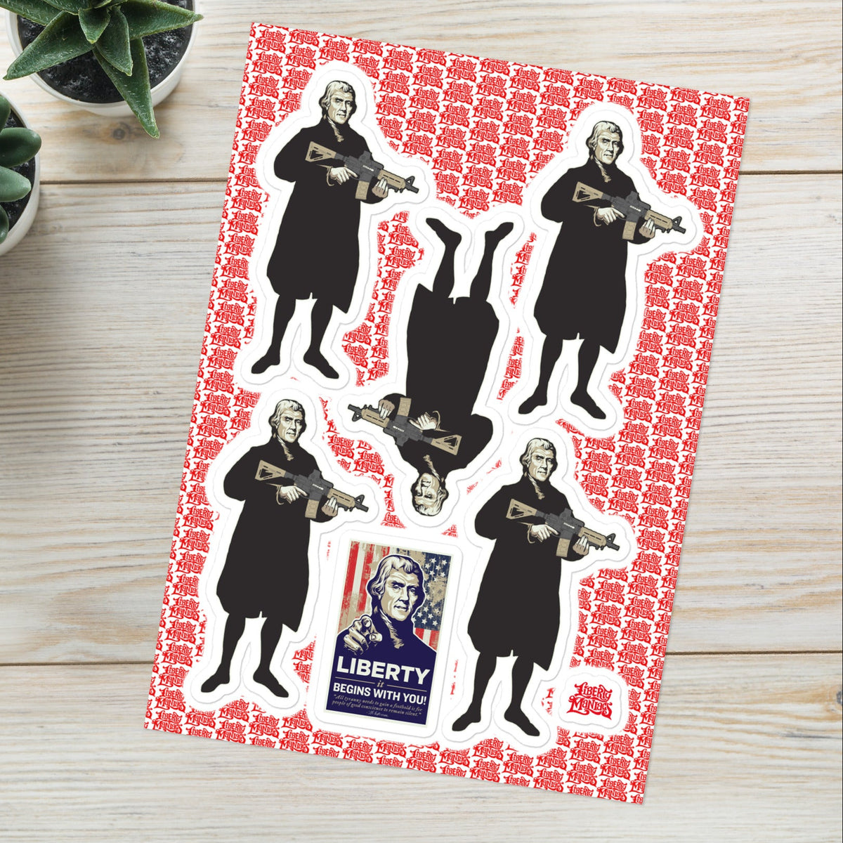 Sheet of stickers with Thomas Jefferson holding a gun design on a red background, placed on a wooden surface with plants.
