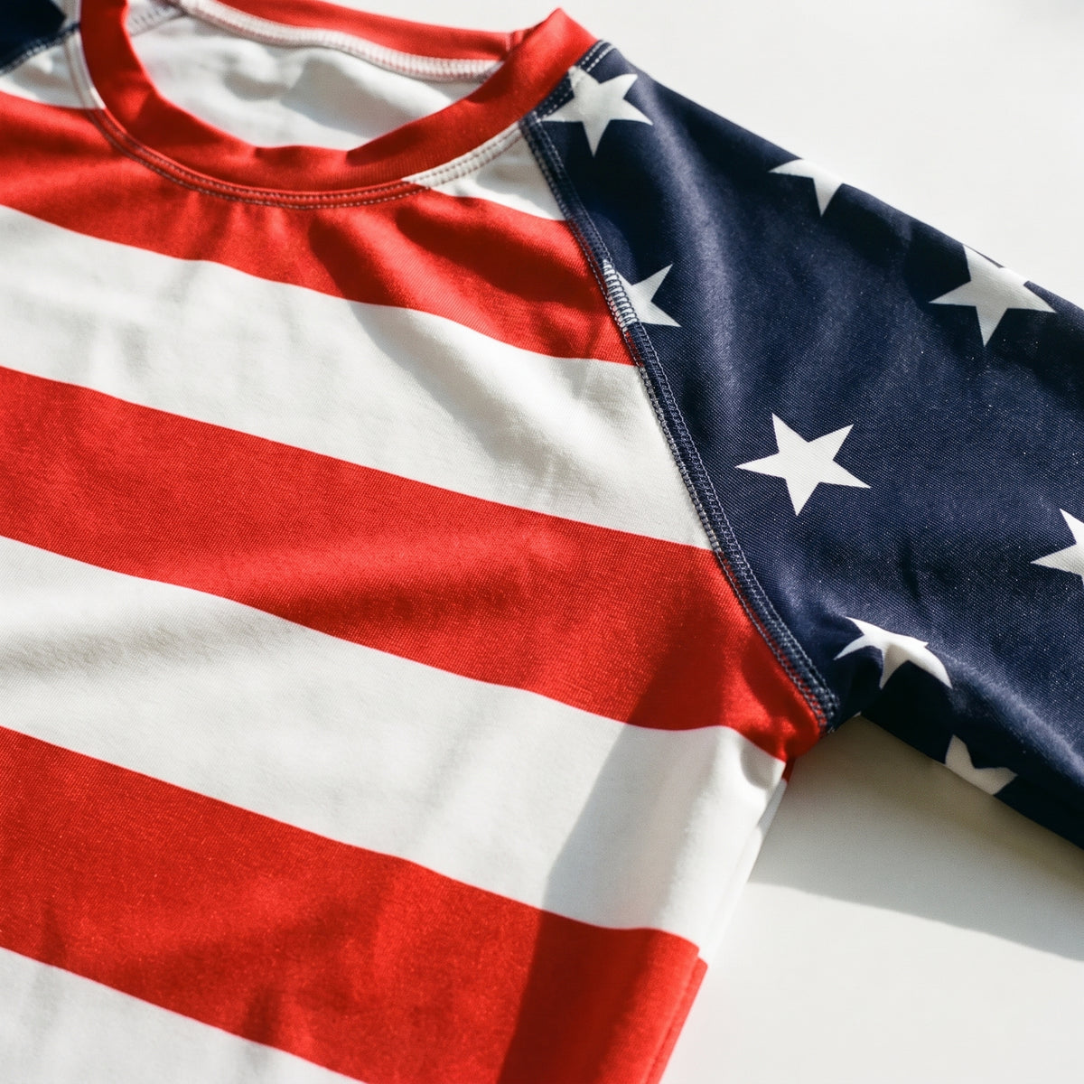 Close-up of a raglan-style t-shirt featuring a red and white American flag stripe pattern on the body and a navy blue sleeve with white stars.