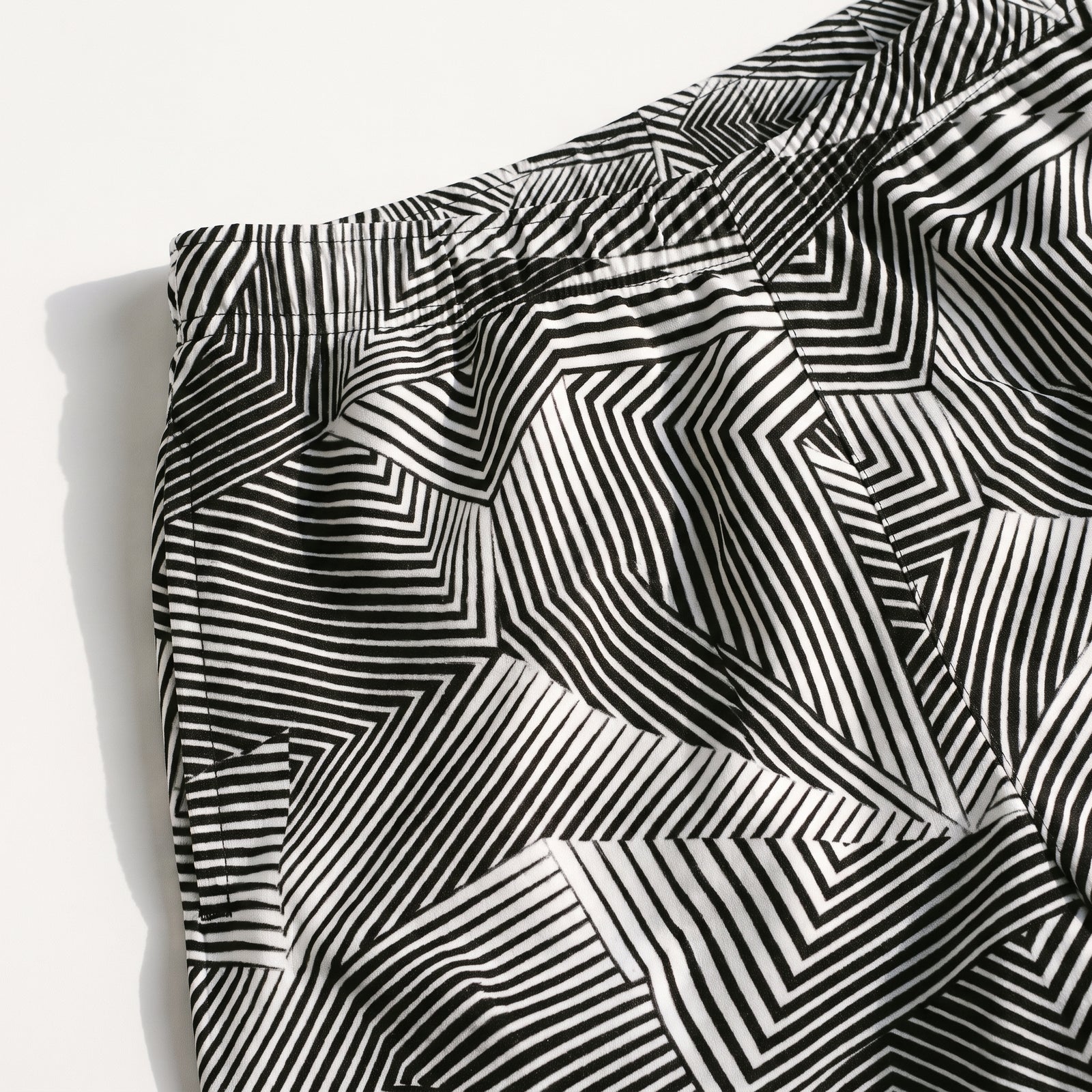 Black and white geometric patterned shorts with an abstract optical illusion stripe design, laid flat on a light gray background.