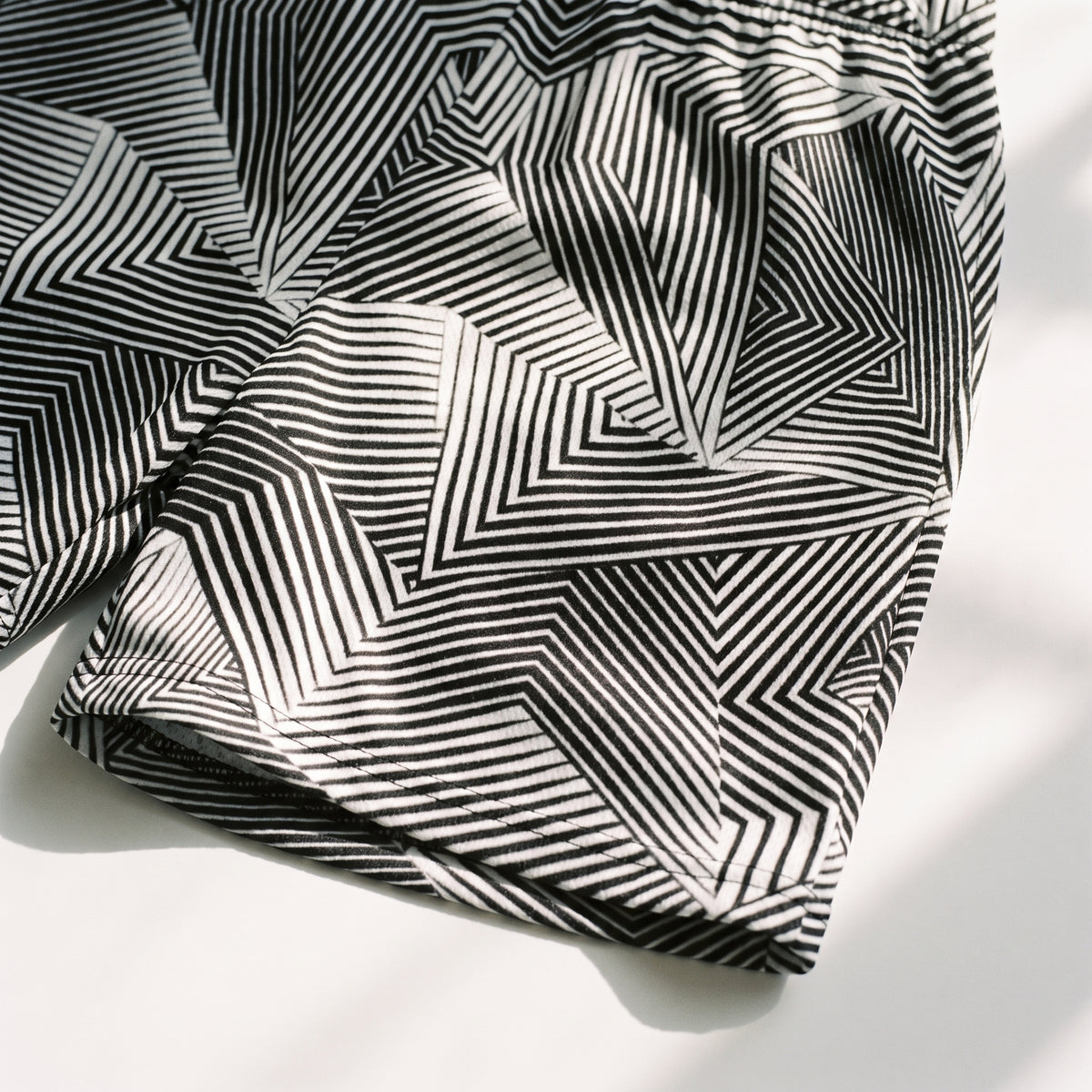 Black and white geometric striped shorts with an optical illusion pattern, laid flat on a white surface with soft shadows.