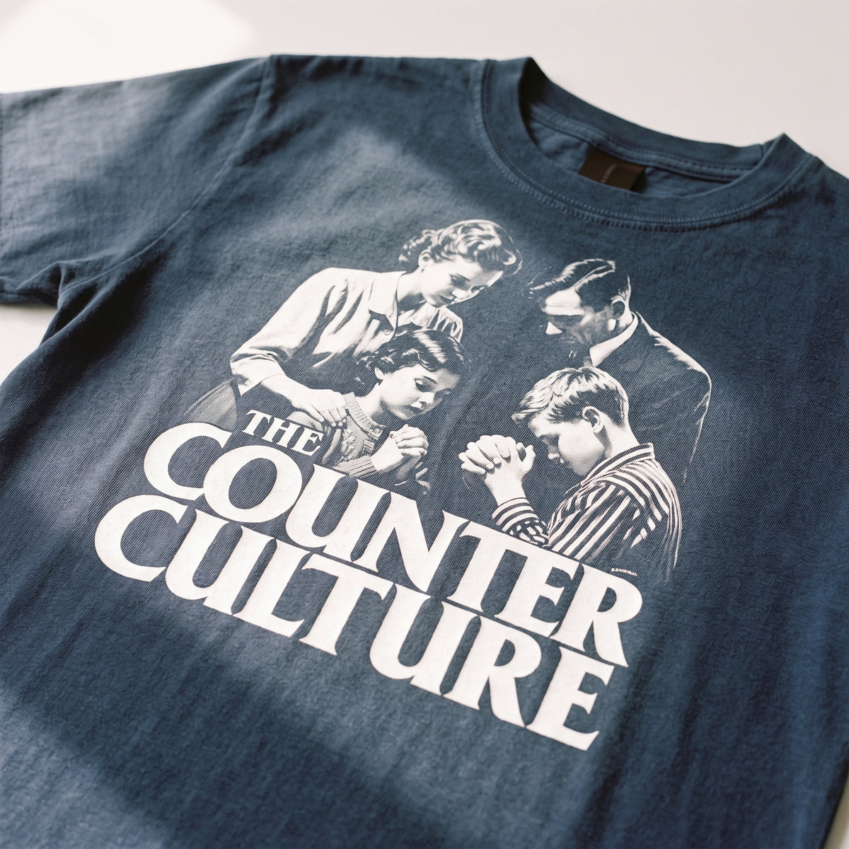 A close-up of a dark blue t-shirt featuring a vintage-style black and white graphic print of four people with the text 'THE COUNTER CULTURE' in large white letters.