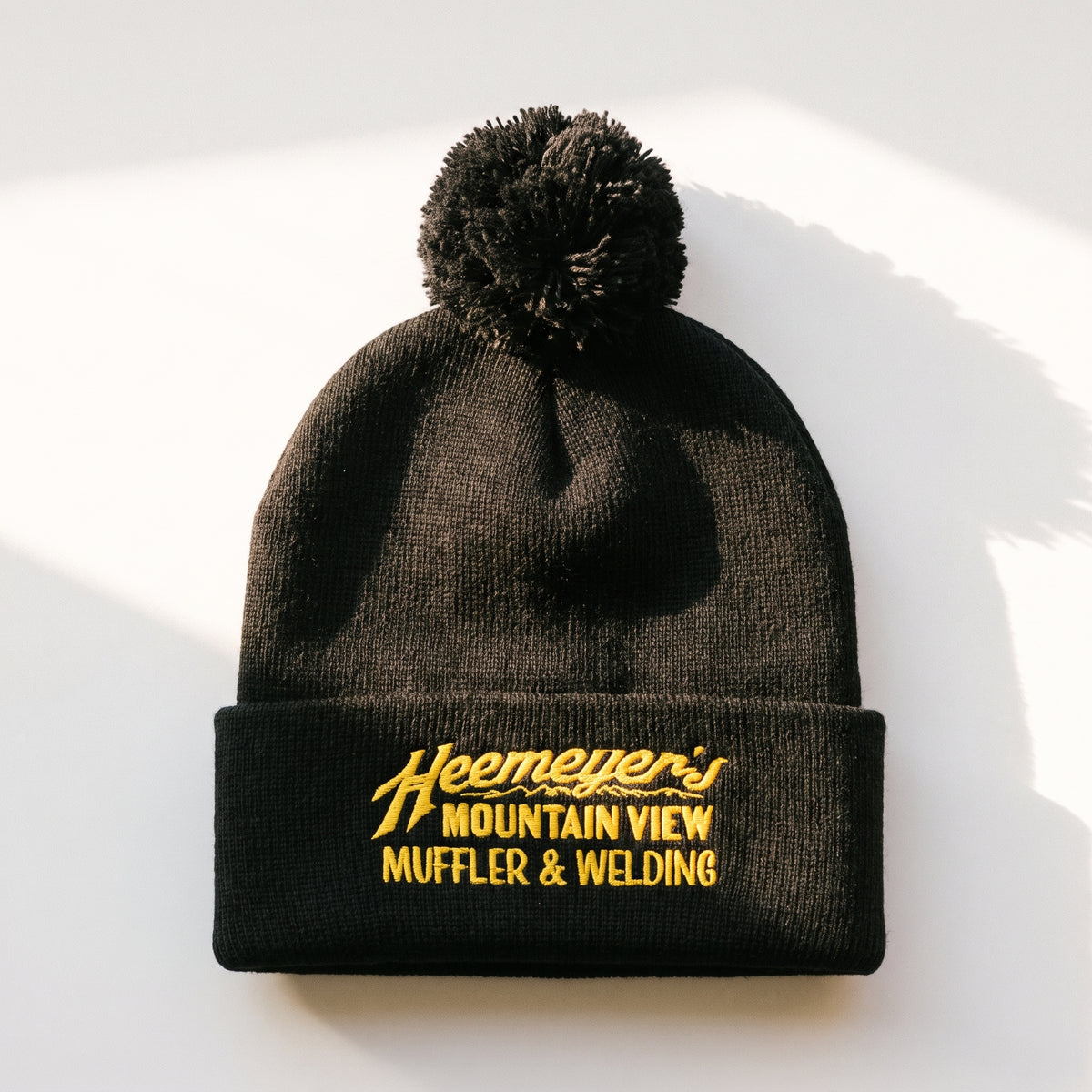 Black Heemeyer’s Mountain View Muffler embroidered pom-pom beanie, full flat lay on white