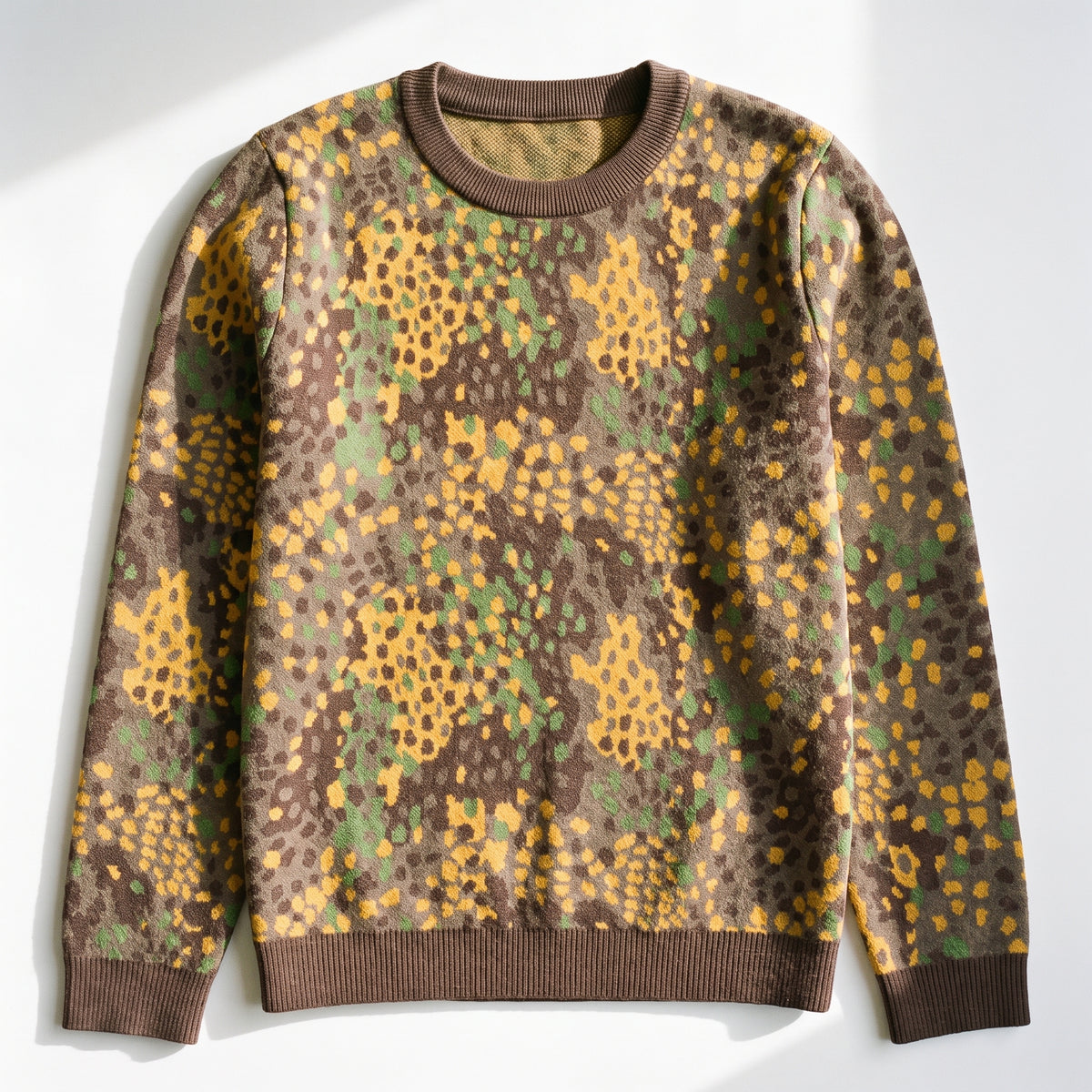 A crewneck sweatshirt with a brown, yellow, and green abstract spotted pattern, laid flat on a white background with soft diagonal shadows.