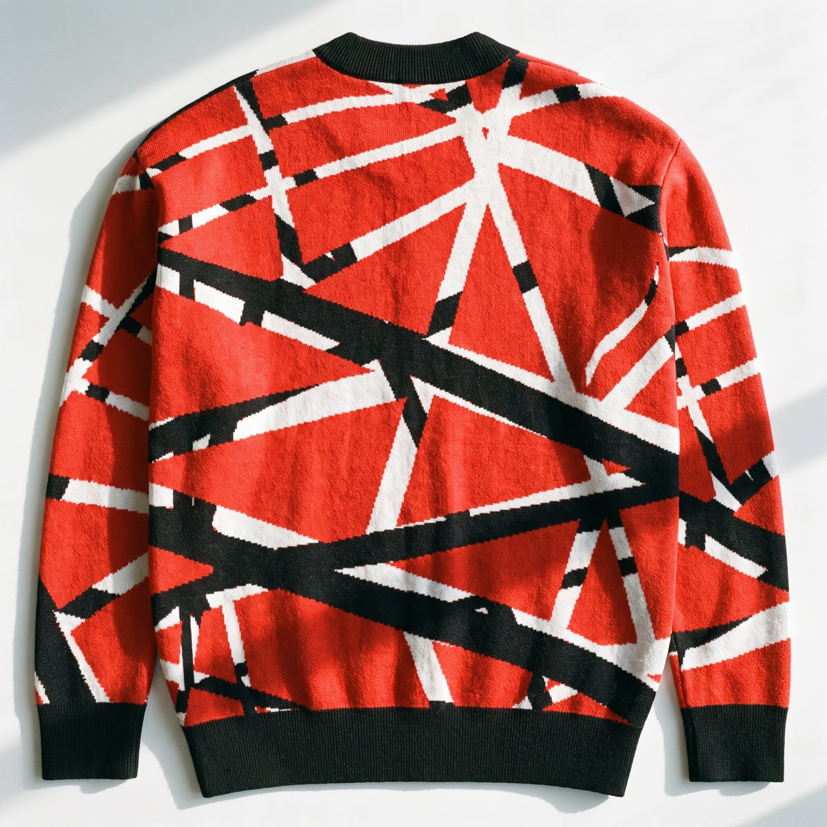 A red knit sweater with a bold black and white geometric line pattern, laid flat against a white background with soft shadows.