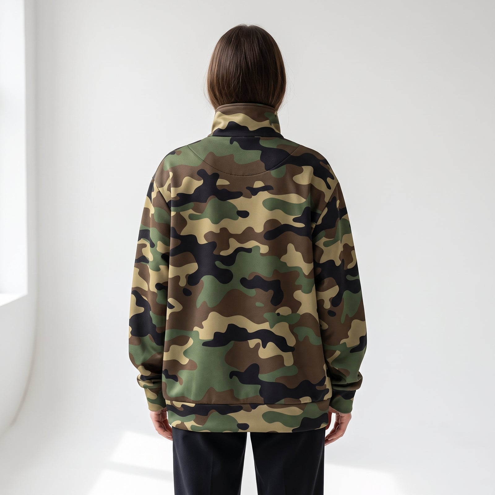 A person viewed from the back wearing a camouflage quarter-zip sweatshirt and black pants in a bright, minimalist white room.