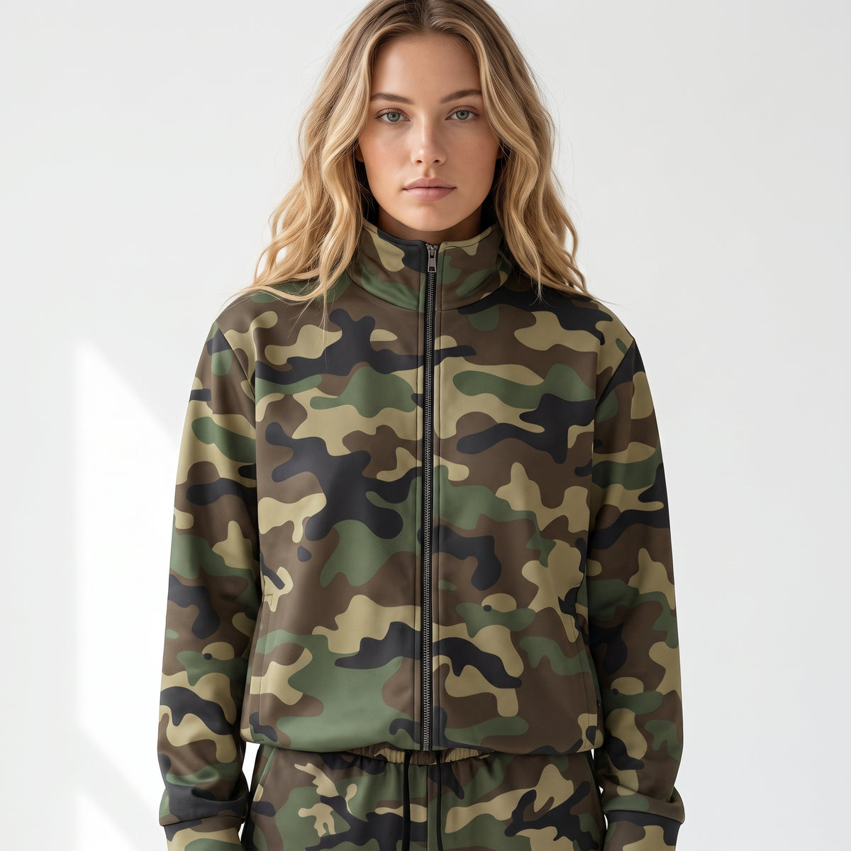 A woman wearing a camouflage zip-up jacket and matching camouflage pants, photographed against a clean light gray studio background.