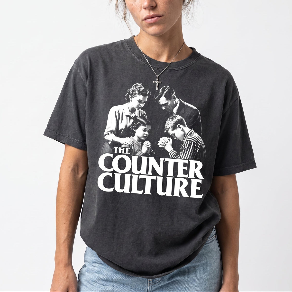 A woman wearing a faded black graphic t-shirt featuring a black and white print of the band Counter Culture with the text 'THE COUNTER CULTURE' in bold white letters, paired with light wash blue jeans against a plain white background.