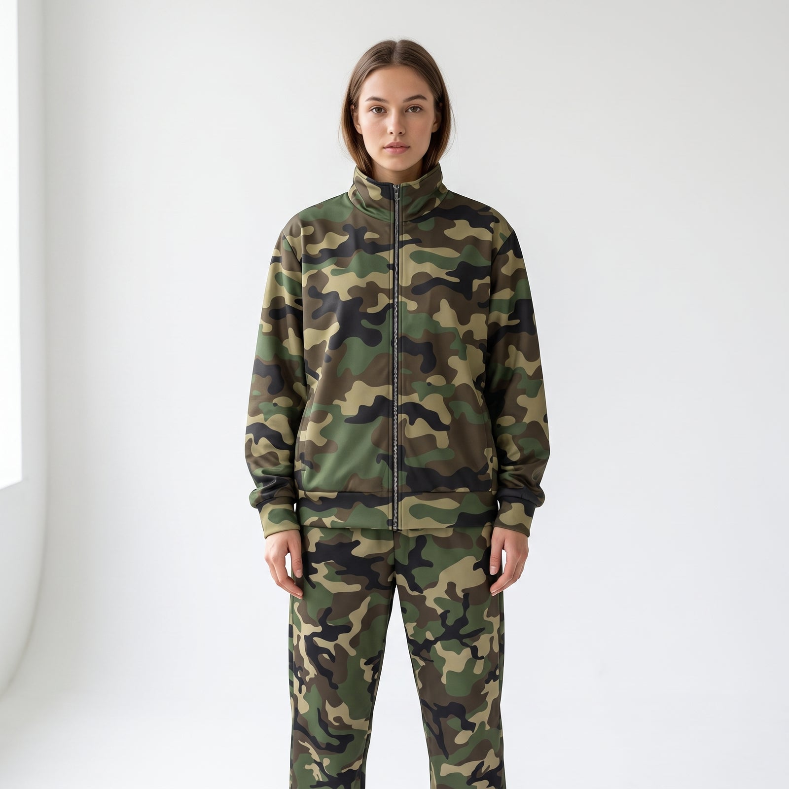 A model stands against a plain white studio background wearing a matching camouflage zip-up jacket and camouflage pants.